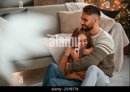 Der Mann umschließt seine Frau von hinten. Ein schönes junges Paar feiert zu Hause Neujahr. Stockfoto