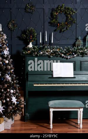 Grüne, pianoblaue Wand mit weihnachtsbaumdekor. Klassische weihnachtsfotozone mit Klavier Stockfoto