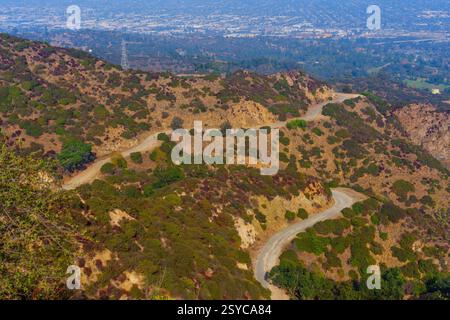 Aus der Vogelperspektive auf gewundenen Wegen durch üppiges Laub im Griffith Park, Kalifornien, mit Panoramablick auf die urbane Landschaft darunter. Stockfoto