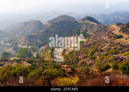 Malerische Aussicht auf Wanderer, die sich auf gewundenen Wegen im Griffith Park bewegen, vor dem Hintergrund der trüben Stadtlandschaft und sanften Hügeln. Stockfoto