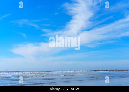Dramatische Wolkenmuster erstrecken sich über den Himmel am Ozean und reflektieren das ruhige Wasser und schaffen eine malerische Küstenatmosphäre. Stockfoto