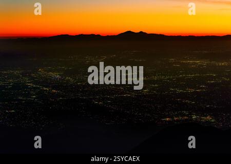 Atemberaubender Blick in die Dämmerung auf das San Bernardino Valley von Rimforest, Kalifornien, mit Blick auf glitzernde Lichter der Stadt vor einem farbenfrohen Sonnenuntergang. Stockfoto