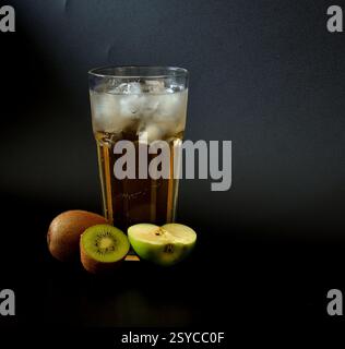 Hohes Glas Fruchtsaftmischung mit Eis auf schwarzem Hintergrund, reife Apfelstücke und Kiwi in der Nähe. Nahaufnahme. Stockfoto