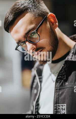 Selbstbewusster junger Mann, der eine Brille mit stilvollem Outfit und neutralem Ausdruck trägt Stockfoto