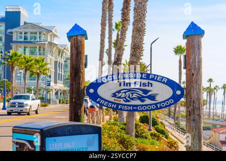 Oceanside, Kalifornien - 27. Dezember 2024: Schild mit Tin Fish Restaurant am Oceanside Pier mit vorbeifahrenden Autos und Palmen im Blick. Stockfoto