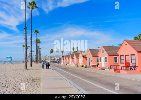 Oceanside, Kalifornien - 27. Dezember 2024: Reihe von bezaubernden Lachsstrand Cottages entlang der Oceanside Promenade, mit Palmen und Strand. Stockfoto