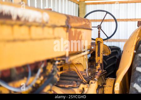 Gelber Traktor mit rostfreiem Lenkrad. Der Traktor steht in einer Scheune Stockfoto