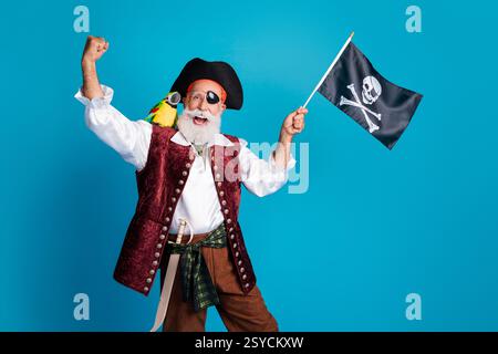 Foto-Porträt des alten lustigen Piraten männlich gewinnende Wellenfahne gekleidete Karnevalsparty Kostümparty isolierter blauer Hintergrund Stockfoto
