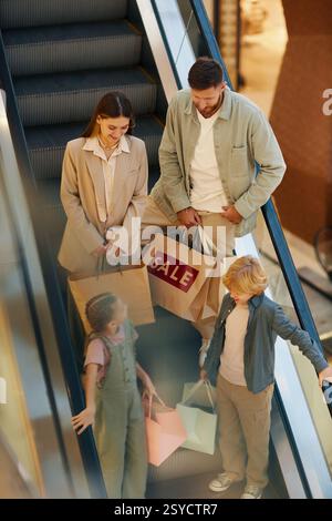 Vertikale Hochwinkelaufnahme der Familie mit riesigen Papiertüten in den Händen, die sich auf der Rolltreppe unterhalten, während sie hinuntergeht Stockfoto