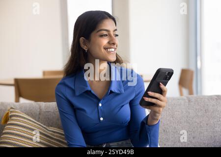 Nachdenkliche Frau, die mit Smartphone auf der Couch sitzt Stockfoto