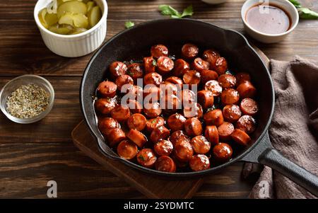 BBQ geräucherte Würstchen in gusseiserner Pfanne auf Holztisch. Nahansicht Stockfoto