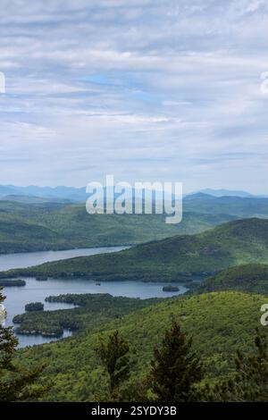 Ein atemberaubender Blick auf einen blauen See mit kleinen bewaldeten Inseln, eingebettet in grüne Berge, mit Schichten entfernter blauer Bergketten Stockfoto