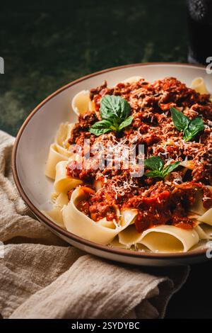 Ein herzhafter Teller Pappardelle-Pasta mit reichhaltiger Bolognese-Fleischsauce, garniert mit frischen Basilikumblättern und geriebenem Parmesankäse. Stockfoto
