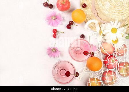 Trendiges Sommerbanner auf hellem Hintergrund. Strohhut, Früchte in Öko-Tasche, erfrischende alkoholische Getränke und Kamillenblüten auf sonnigem Tisch. Urlaub Stockfoto