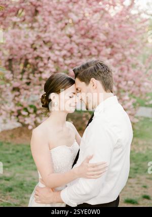 Ein Mann und eine Frau teilen einen zärtlichen Moment, umgeben von leuchtenden rosa Blüten, die ihre Liebe im Frühling festhalten. Stockfoto
