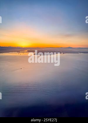 Blick aus der Vogelperspektive auf das Meer mit kleinen Inseln bei Sonnenaufgang. Das goldene Leuchten reflektiert das Wasser und verbindet warme und kühle Töne über die weite Küste Stockfoto