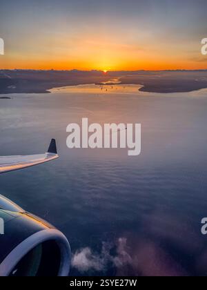 Aus der Vogelperspektive des Ozeans und der Inseln bei Sonnenaufgang. Der Flugzeugflügel reflektiert die goldenen Töne des frühen Morgenlichts über dem Stockfoto