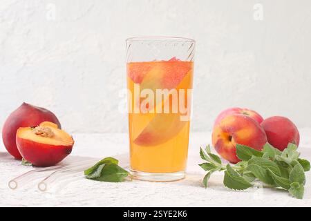 Eistee oder Cocktail mit Pfefferminze und Lobdom, Rezept für erfrischendes Sommergetränk. Glas mit Pfirsichfrucht-Limonade auf leichtem Betontisch, Entgiftungsdiät Stockfoto