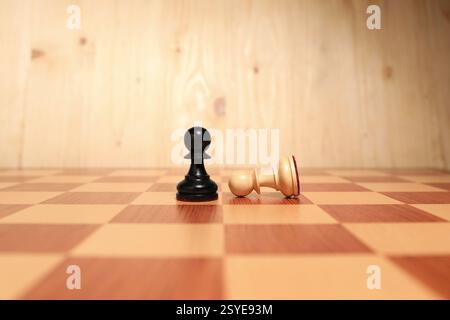 Schwarzer Bauernhof nahe gefallenem Weißen mitten auf dem Schachbrett. Wettbewerbskonzept Stockfoto