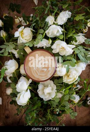 Cappuccino und Blumenkomposition. Morgenkaffee und wunderschöne Rosenblumen auf einem hölzernen Hintergrund, Blick von oben. Gemütliches Frühstück. Flacher STYLE. Stockfoto