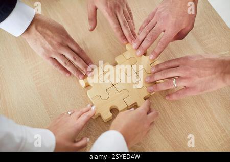 Draufsicht zugeschnittene Hände einer Gruppe von Geschäftsleuten, die Holzpuzzle zusammenbauen. Stockfoto