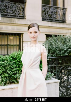 Eine stilvolle junge Frau steht selbstbewusst in einem wunderschönen Kleid, umgeben von Grün in einer urbanen Umgebung. Stockfoto