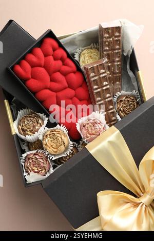 Verschiedene köstliche Schokoladenbonbons in Box auf beigem Hintergrund, Blick von oben Stockfoto