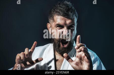 Karate-Mann. Nahaufnahme Porträt eines professionellen Karatelehrers in weißem Kimono. Starker bärtiger Karatekämpfer, der sich auf den Wettkampf im Fitnessstudio vorbereitet. Wütend Stockfoto
