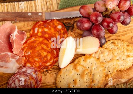 Eine hölzerne Platte mit Essen mit Crackern, Trauben und Äpfeln. Die Cracker befinden sich auf der rechten Seite des Tellers und die Trauben und Äpfel auf der linken Seite Stockfoto