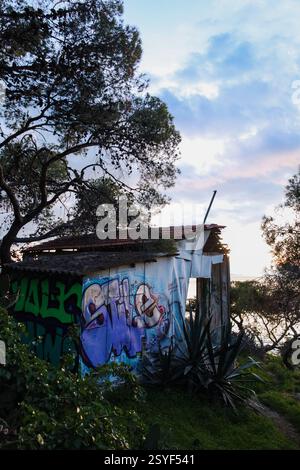 Vouliagmeni, Griechenland - 28. Februar 2025. Ein altes, baufälliges Holzhaus mit kaputten Fenstern und Graffiti an den Wänden am Paragkes Beach Stockfoto