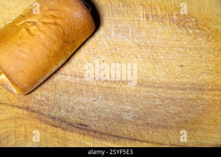 Ein warmer Brotlaib wird auf ein glattes Holzschneidebrett gelegt. Die Kruste ist goldbraun und zeigt ein frisches, hausgemachtes Aussehen. Perfekt für Servietten Stockfoto