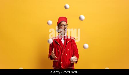 Entertainer in rotem Anzug, der mit Bällen vor gelbem Hintergrund jongliert Stockfoto