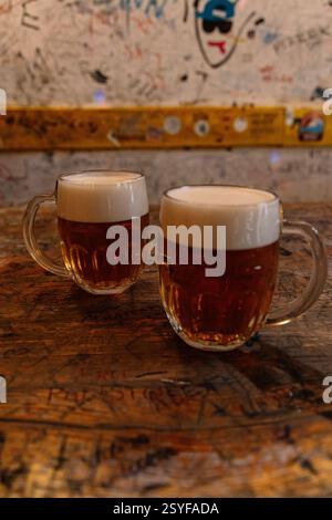17.02.2025, Budapest. In einer Ruinbar in Budapest, Ungarn, mit einer Graffiti-bedeckten Wand, sitzen zwei Schaum-Bierbecher auf einem zerkratzten Holztisch Stockfoto