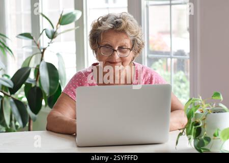Ältere Frau, die am Schreibtisch sitzt und einen Laptop benutzt Stockfoto