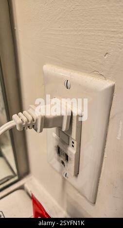 Das Netzkabel ist fest in eine weiße Wandsteckdose neben einem Spiegel eingesteckt. Die Steckdose verfügt über mehrere Steckdosen und ein klares, modernes Design, das typisch für das Design ist Stockfoto