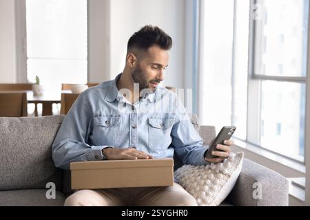 Mann, der die Box hält, mit dem Smartphone, überprüfen Sie die Lieferdetails Stockfoto