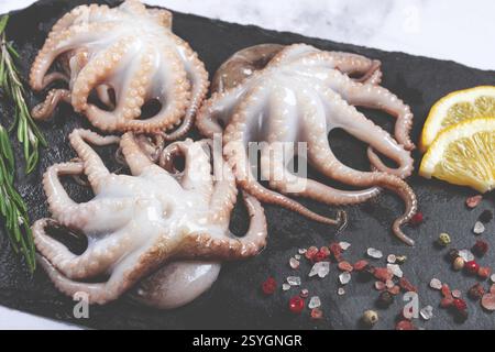 Frischer Krake, auf schwarzem Schiefer, mit Zitrone und Grün, Blick von oben, keine Leute Stockfoto