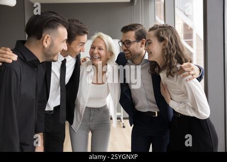Fröhliche Teamkollegen stehen im Büro, umarmen Schultern und fühlen Einheit Stockfoto