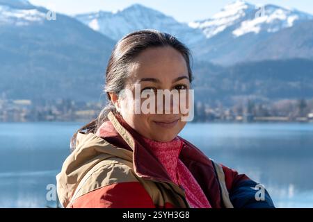 Eine 40-45-jährige Frau in warmen Kleidern, die vor einer Berglandschaft und einem See lächelt Stockfoto