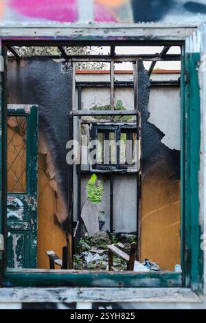 Vouliagmeni, Griechenland - 28. Februar 2025. Ein Fensterrahmen zeigt ein verbranntes, zerstörtes Inneres eines verlassenen Holzhauses Stockfoto