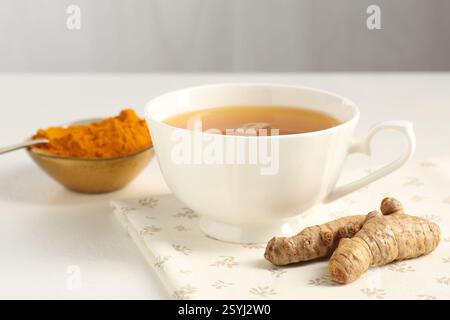 Aromatischer Kurkuma-Tee, Pulver und Rhizome auf weißem Tisch, Nahaufnahme Stockfoto