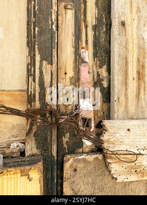 Altes, kaputtes Holztor am abgebrochenen Haus. ‚Geschlossen‘ mit rostigem Metalldraht. Stockfoto