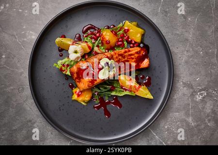Köstlicher gegrillter Lachs mit lebendiger Granatapfelsauce, frischem Gemüse, Zitrusgarnitur und essbaren Blumen, Gourmet-Dining-Konzept Stockfoto