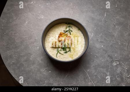 Leckere cremige Suppe mit knusprigen Croutons und Rosmarin, präsentiert in einer Schüssel auf grauem Stein, Vogelperspektive, Gourmet-Menü-Konzept Stockfoto
