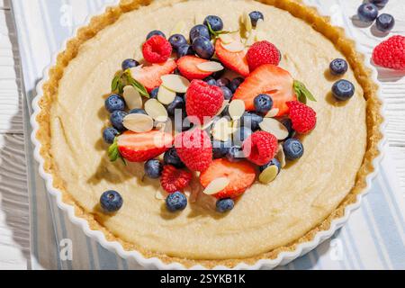 Beerentorte mit Marzipankruste und Kokosnussmandelcreme Füllung in Keramikkuchenplatte auf weißem Holztisch, Nahaufnahme Stockfoto