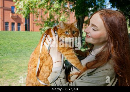 Ingwermädchen mit Ingwerkatze an der Leine im Park Stockfoto