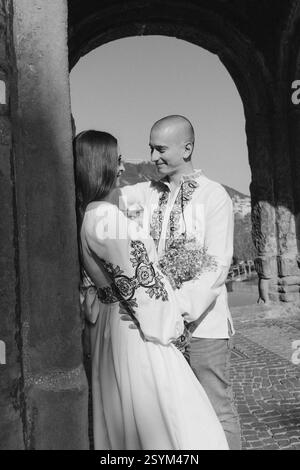 Sommerhochzeit in Georgien: Romantisches Paar in ukrainischen bestickten Outfits küsst sich unter einem alten Bogen Stockfoto