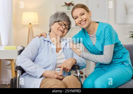 Alte ältere Frau mit körperlicher Behinderung posiert im Rollstuhl in der Nähe einer Krankenschwester Stockfoto