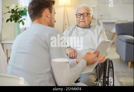 Krankenschwester oder Pflegekraft zeigt Testergebnisse für älteren behinderten Mann im Rollstuhl im Pflegeheim Stockfoto