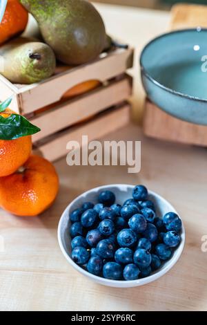 Nahaufnahme von Heidelbeeren, Mandarinen und Birnen auf hölzerner Arbeitsplatte in der rustikalen Küche. Warme und gemütliche Atmosphäre mit natürlichen Texturen und sanftem Licht. Stockfoto